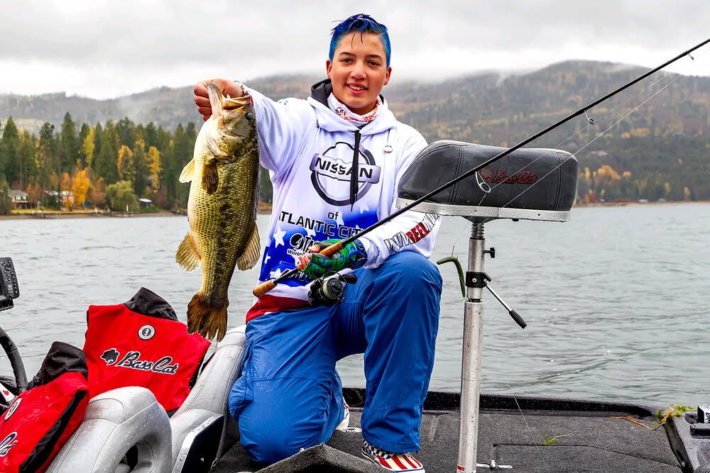 AJ-Max holding a largemouth bass on the bow of a bass boat
